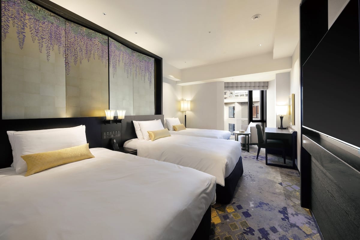 A hotel room with two beds, a desk, and a large artwork on the wall.