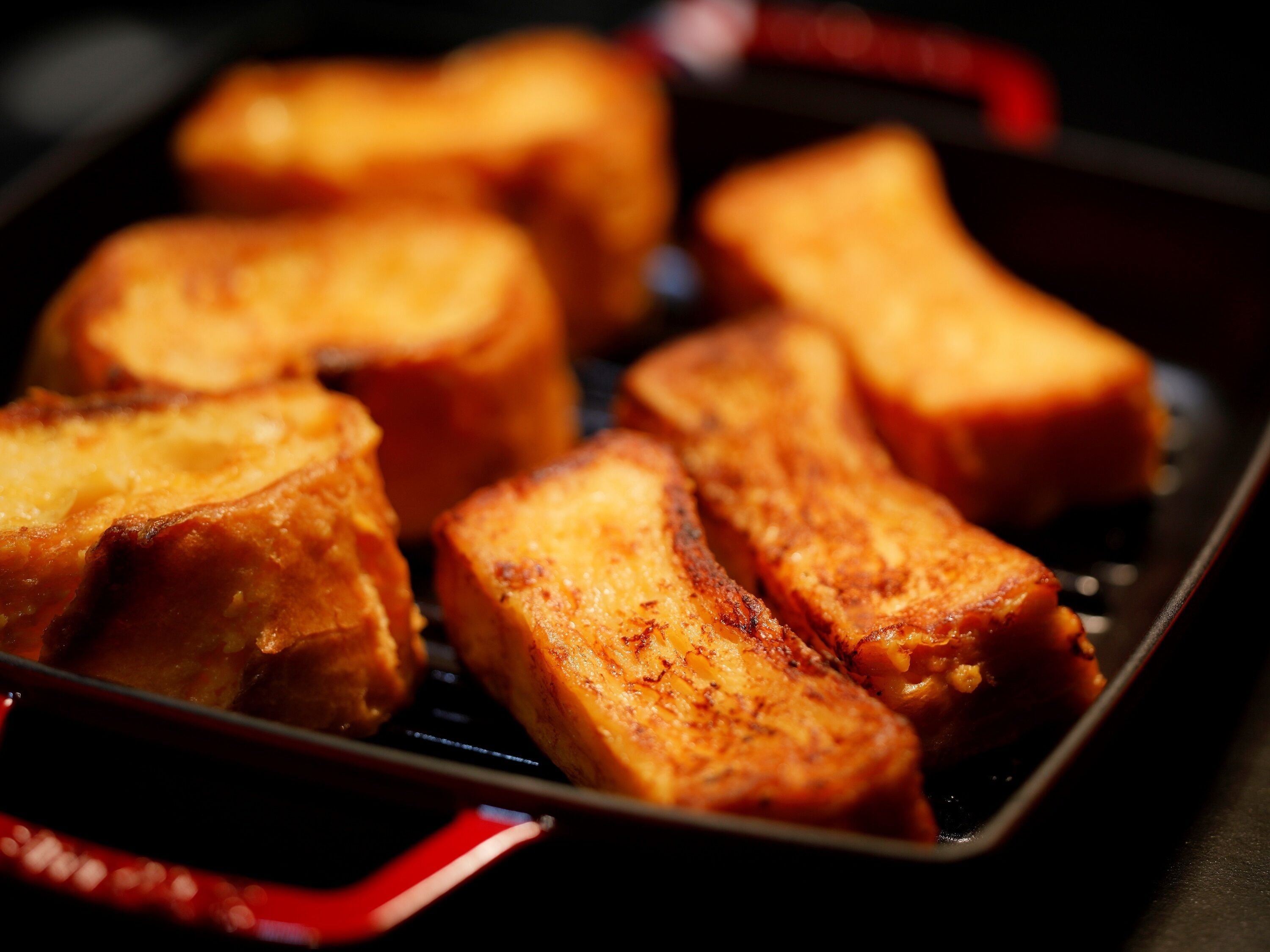 A close-up of golden-brown French toast in a black pan.