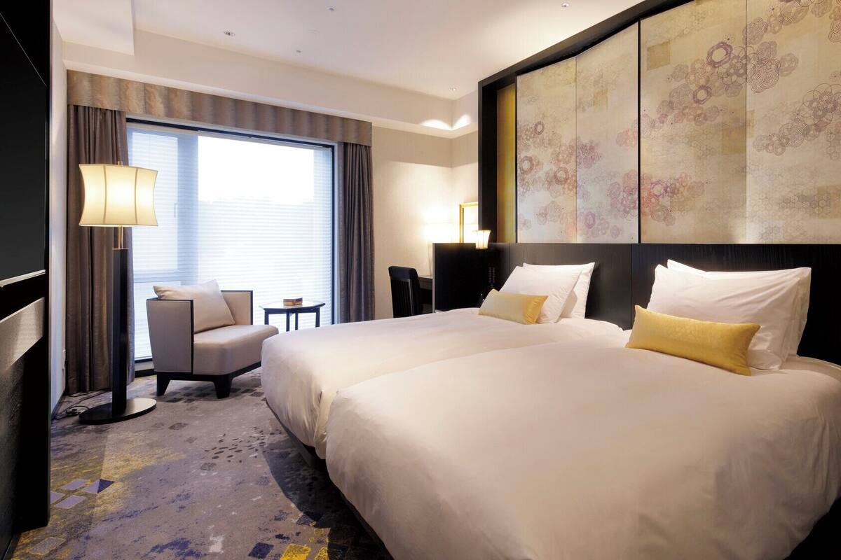 A hotel room with two beds, a desk, a chair, and a large artwork on the wall.