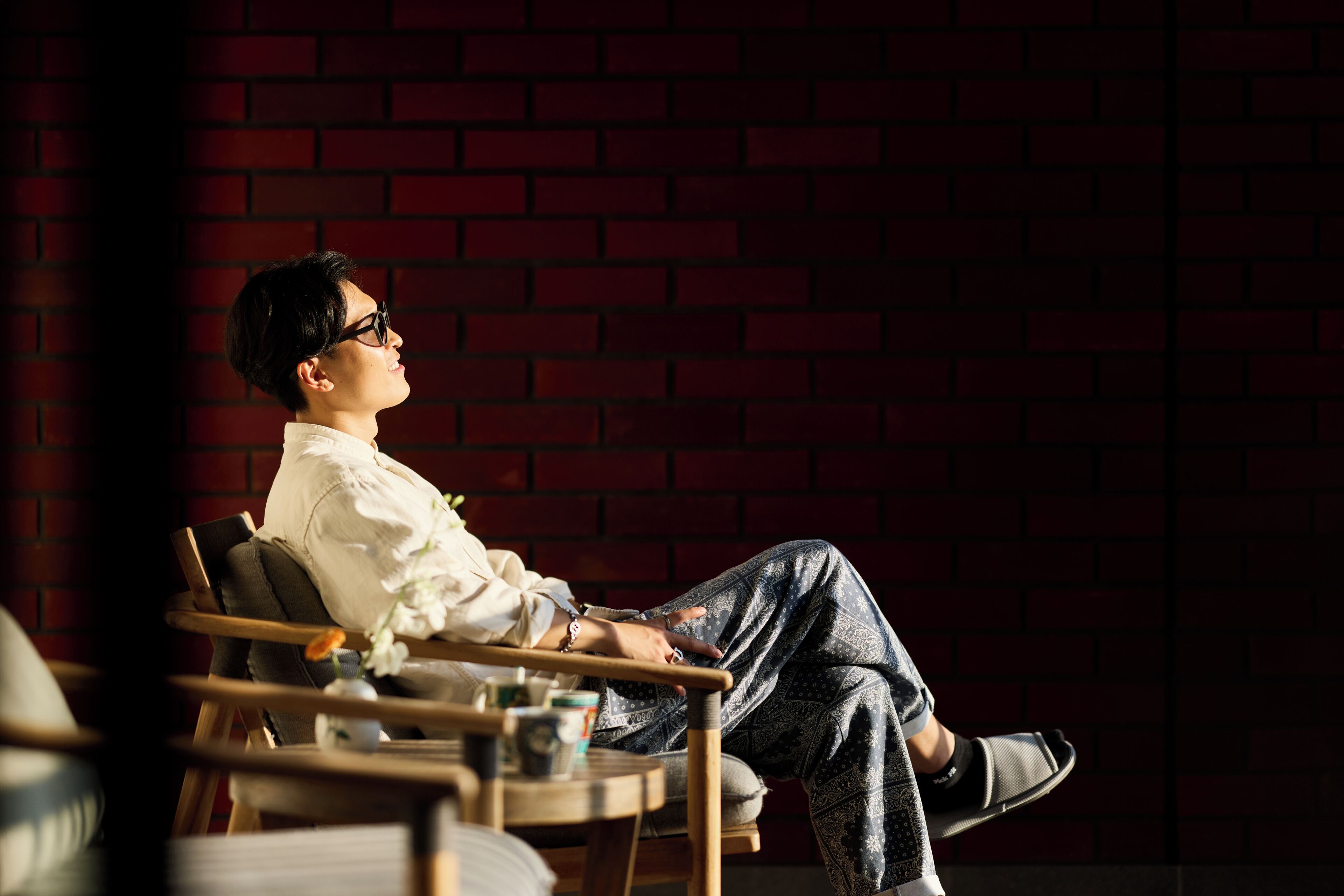 A person seated in a chair with a brick wall background.