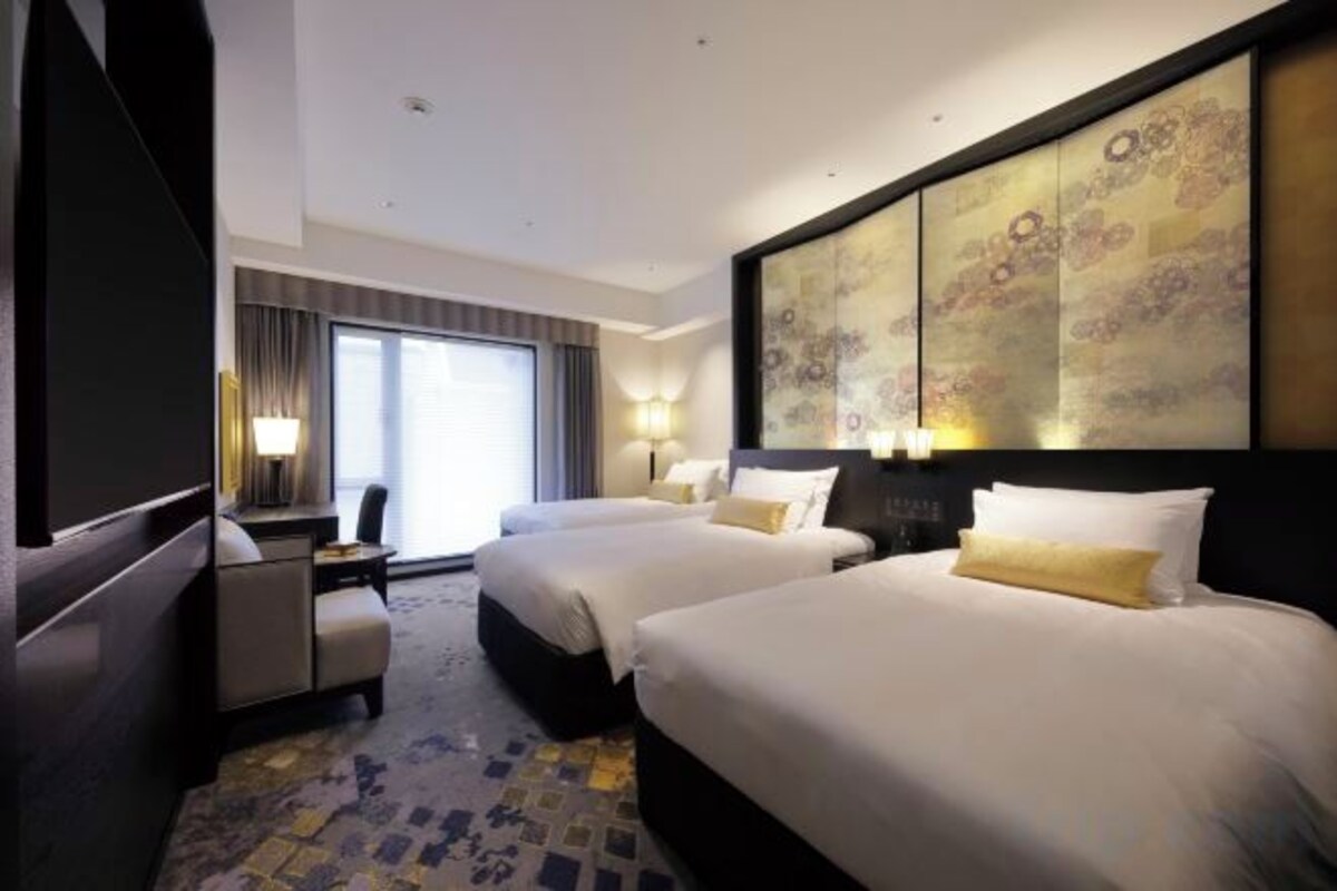 A hotel room with two beds, a desk, and a large window.