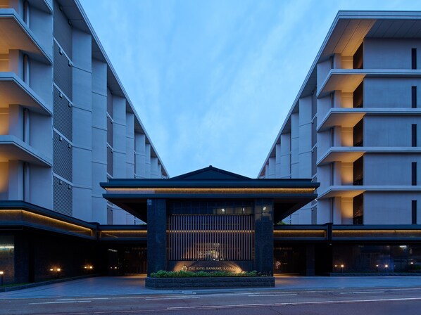 Una entrada de hotel moderna con un pabellón central, grandes ventanales y una fachada bien iluminada.