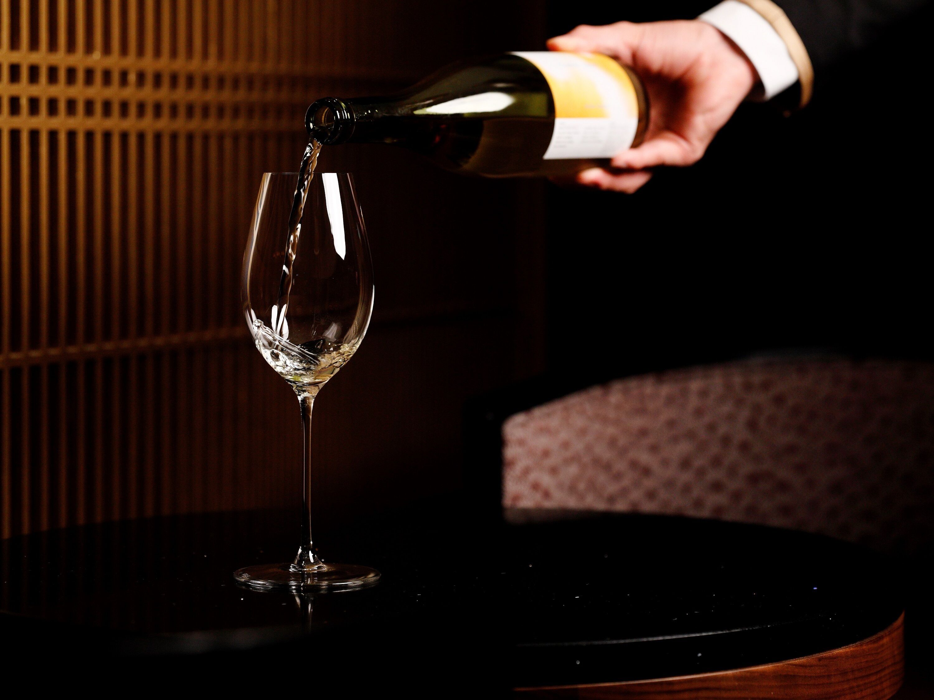Eine Hand gießt Wein in ein Glas auf einem Tisch.