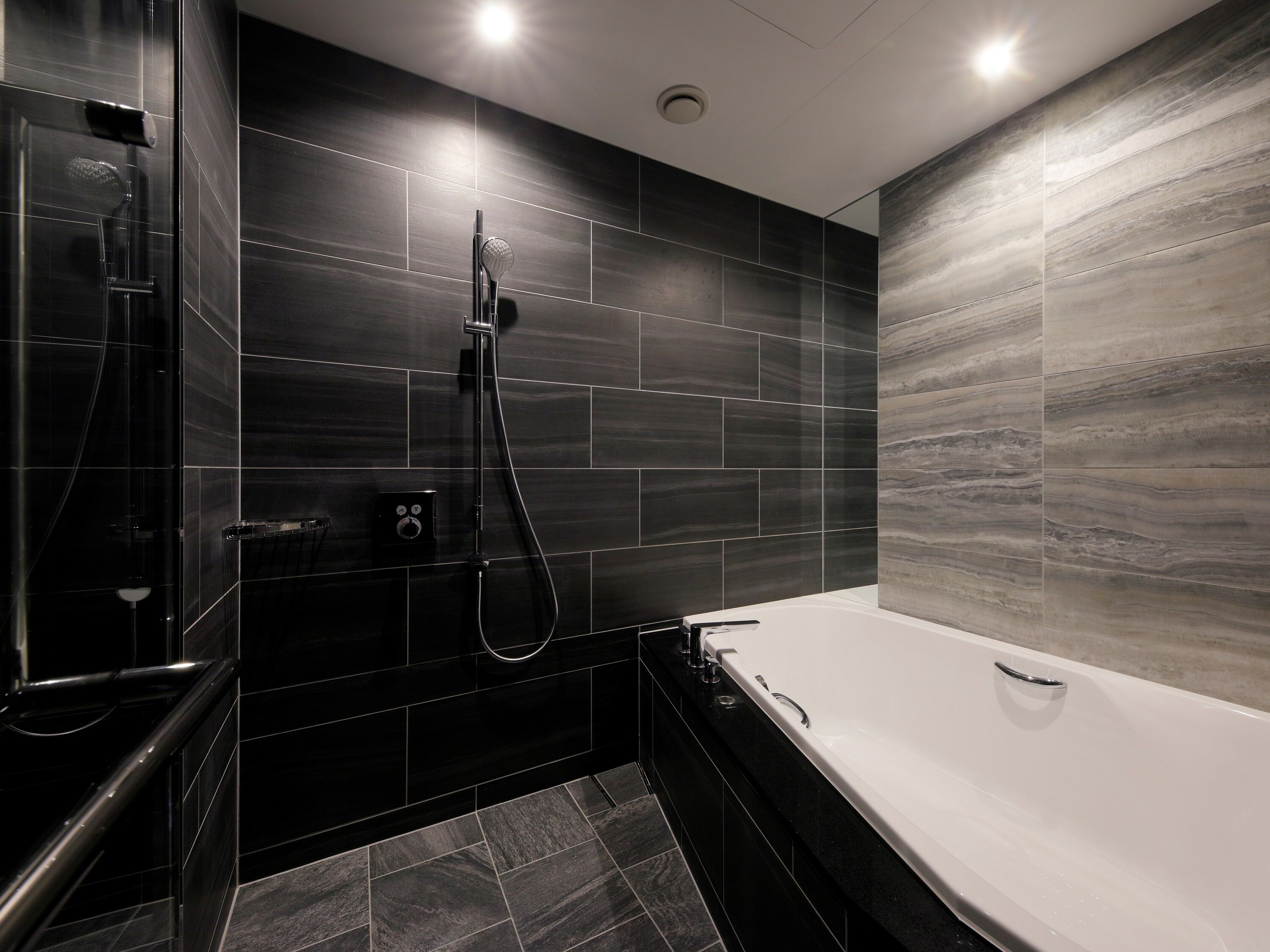 A modern bathroom with a freestanding bathtub, a shower with a handheld showerhead, and a wall-mounted control panel.
