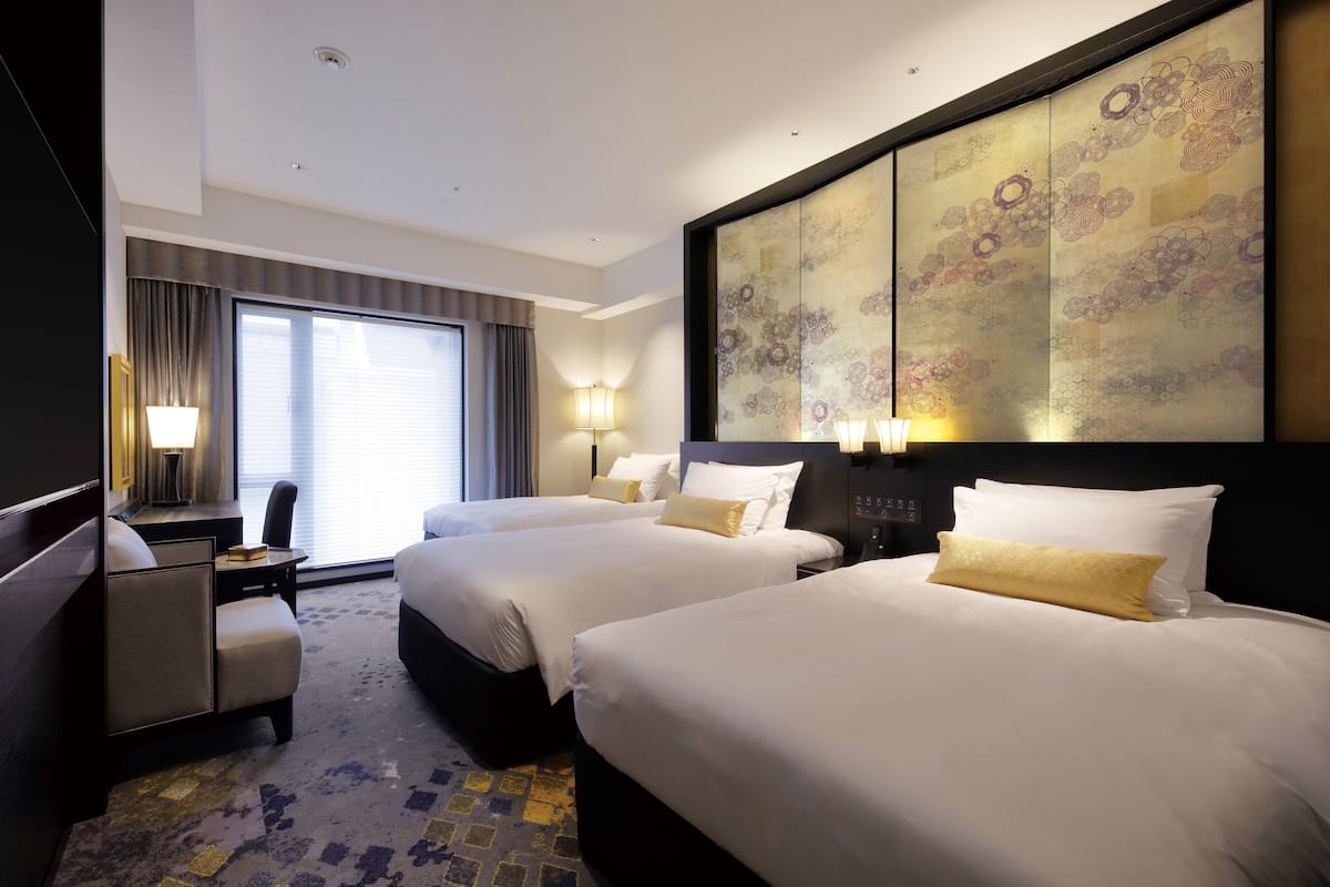 A hotel room with two beds, a desk, a chair, and a large decorative wall panel.