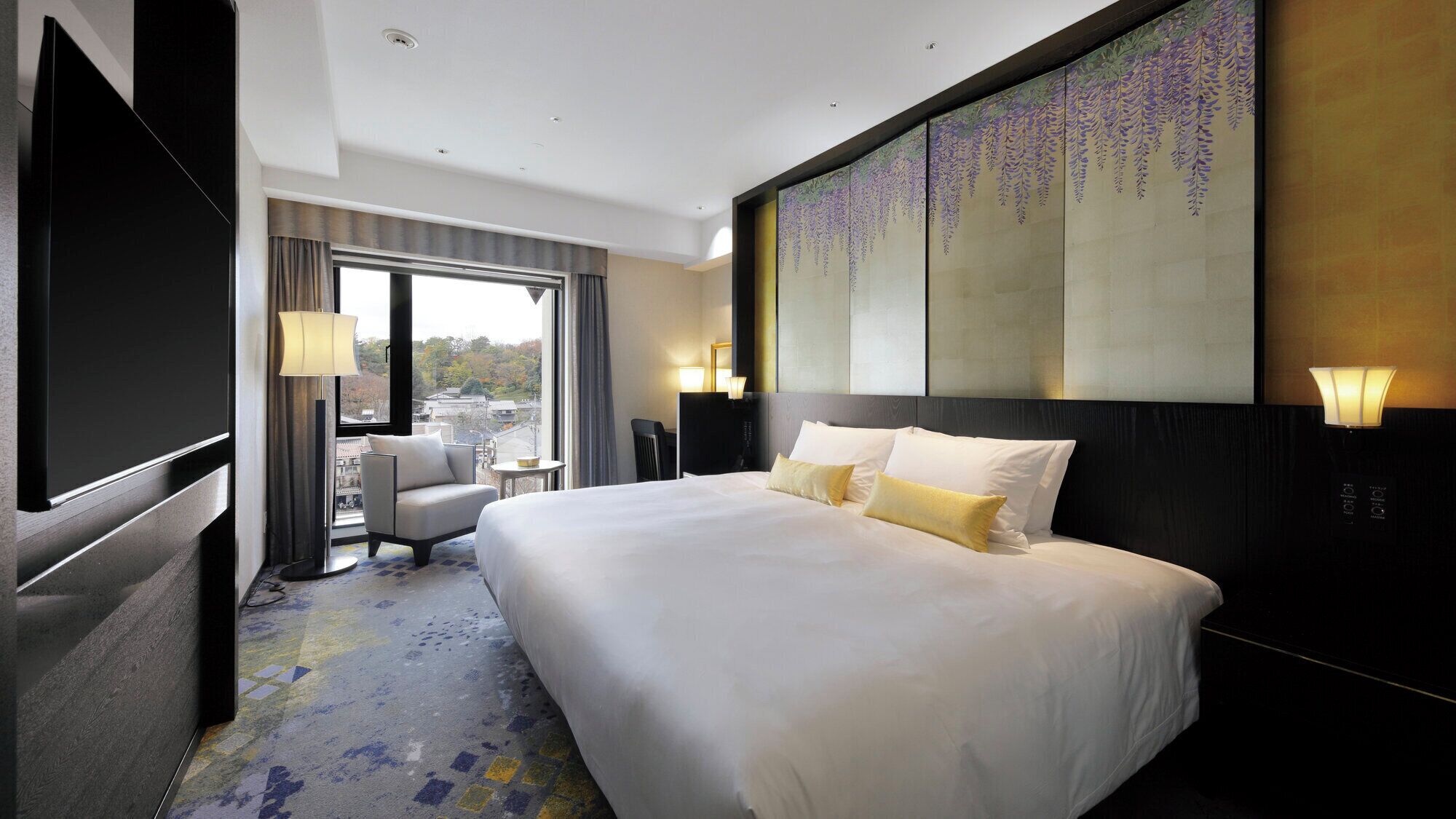 Habitación de hotel con una cama grande, un escritorio, una silla, un televisor y vistas a la ciudad.
