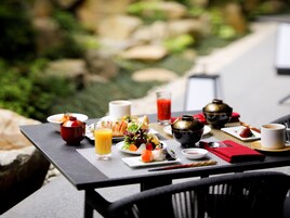 Mesa posta com itens de café da manhã, incluindo um copo de suco de laranja, um prato de sushi, uma xícara de café e uma chaleira.