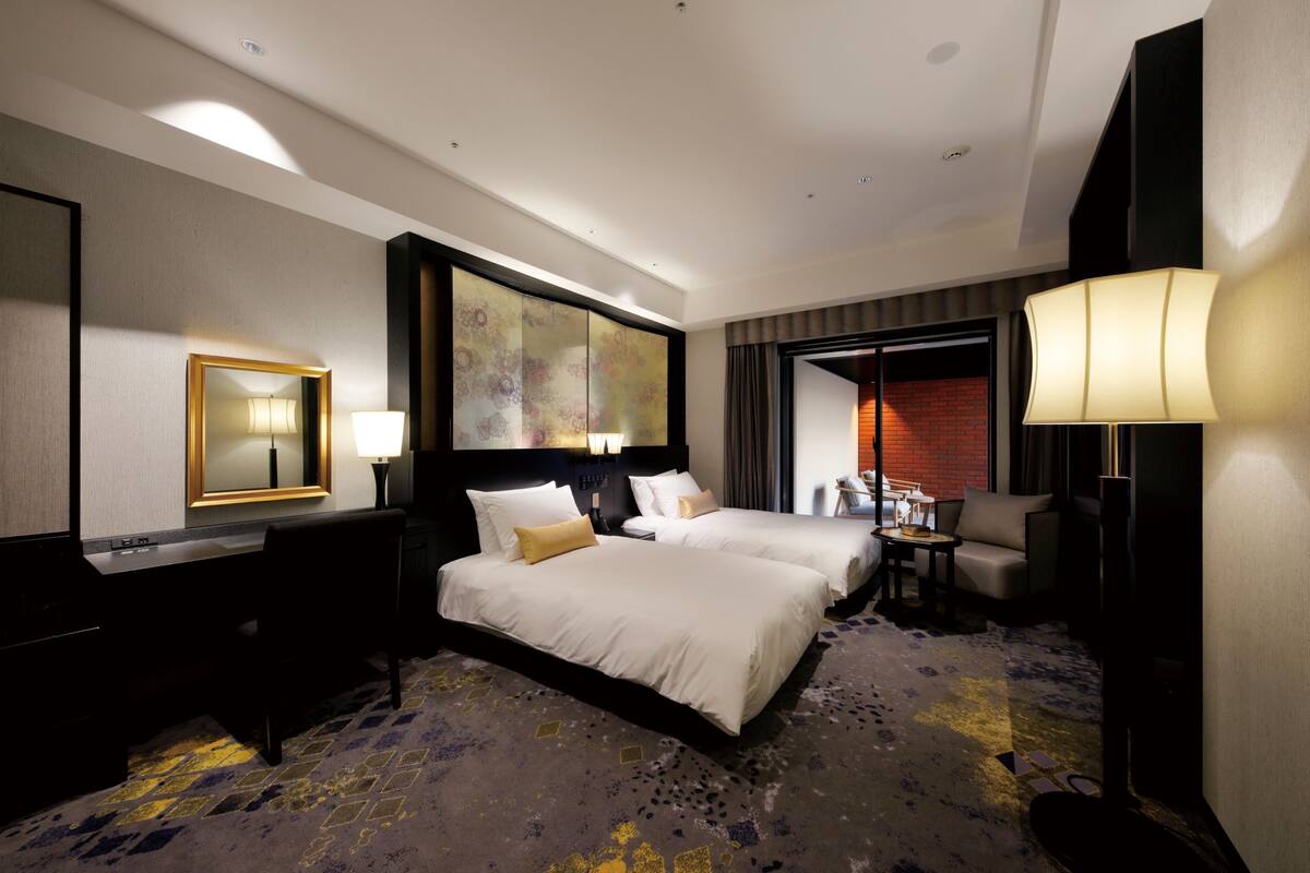 A hotel room with a large bed, a desk, a chair, a lamp, and a painting on the wall.