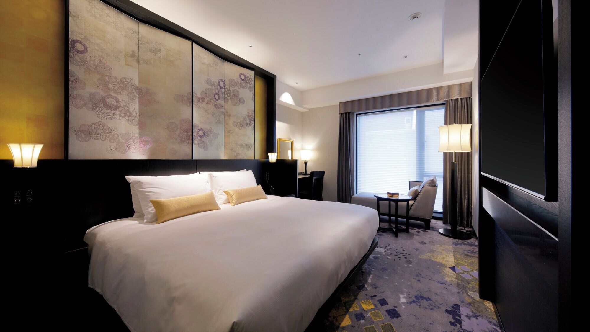 Quarto de hotel com uma cama grande, uma escrivaninha, uma cadeira e uma janela ampla.