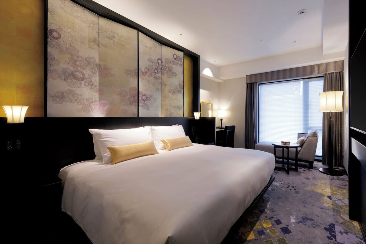 A hotel room with a large bed, a desk, a chair, and a large window.