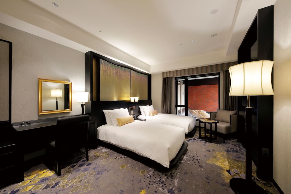 A hotel room with a large bed, a desk, a chair, a TV, and a bathroom visible through an open door.