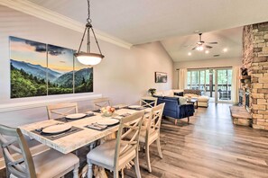 A dining area with a wooden table set for four, a large painting of a mountain landscape, and a stone fireplace in the background.