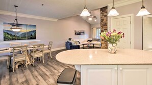 Una cocina moderna con una isla central, iluminación colgante y un comedor con sillas y una mesa de madera.