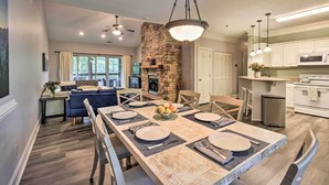 Un comedor amplio con una mesa larga dispuesta para cuatro comensales, una chimenea de piedra y una cocina con electrodomésticos modernos.