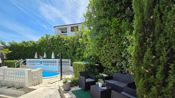 Ein Poolbereich mit einer Steinterrasse, einem weißen Zaun und einer schwarzen Outdoor-Sitzgruppe.
