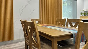 A modern dining area with a wooden table and chairs, a marble wall, and a wooden slat partition. - Spacious 3 Bedrooms with 2 King Beds and 2 Bathrooms (Murray)