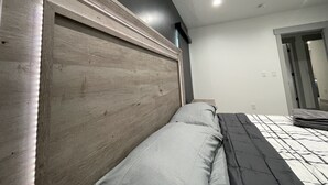 A bedroom with a wooden headboard, a bed with grey and black bedding, and a white ceiling with recessed lighting. - Spacious 3 Bedrooms with 2 King Beds and 2 Bathrooms (Murray)