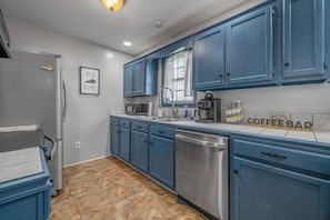 A kitchen with blue cabinets, a dishwasher, a coffee maker, and a sign that says 'COFFEE BAR'.