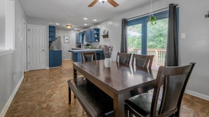 A dining area with a wooden table and chairs, a ceiling fan, and a view of the outdoors through large windows. - Your Kentucky Home (Georgetown)