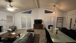 Un salon spacieux doté d’une cheminée, d’un ventilateur de plafond, d’un coin repas avec une table et des chaises, et d’une grande fenêtre offrant une vue dégagée.
