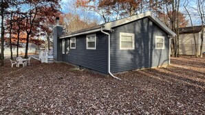 Une maison de plain-pied à l’extérieur sombre, dotée d’une cheminée et d’un petit porche avec deux chaises.