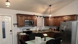 Une cuisine compacte dotée de meubles en bois, d’appareils électroménagers en acier inoxydable et d’un coin repas avec une table en verre et des chaises noires.