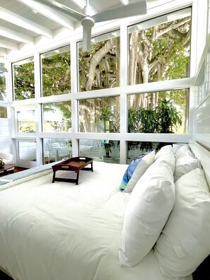Une chambre avec un grand lit, de nombreuses fenêtres et une vue sur les arbres.