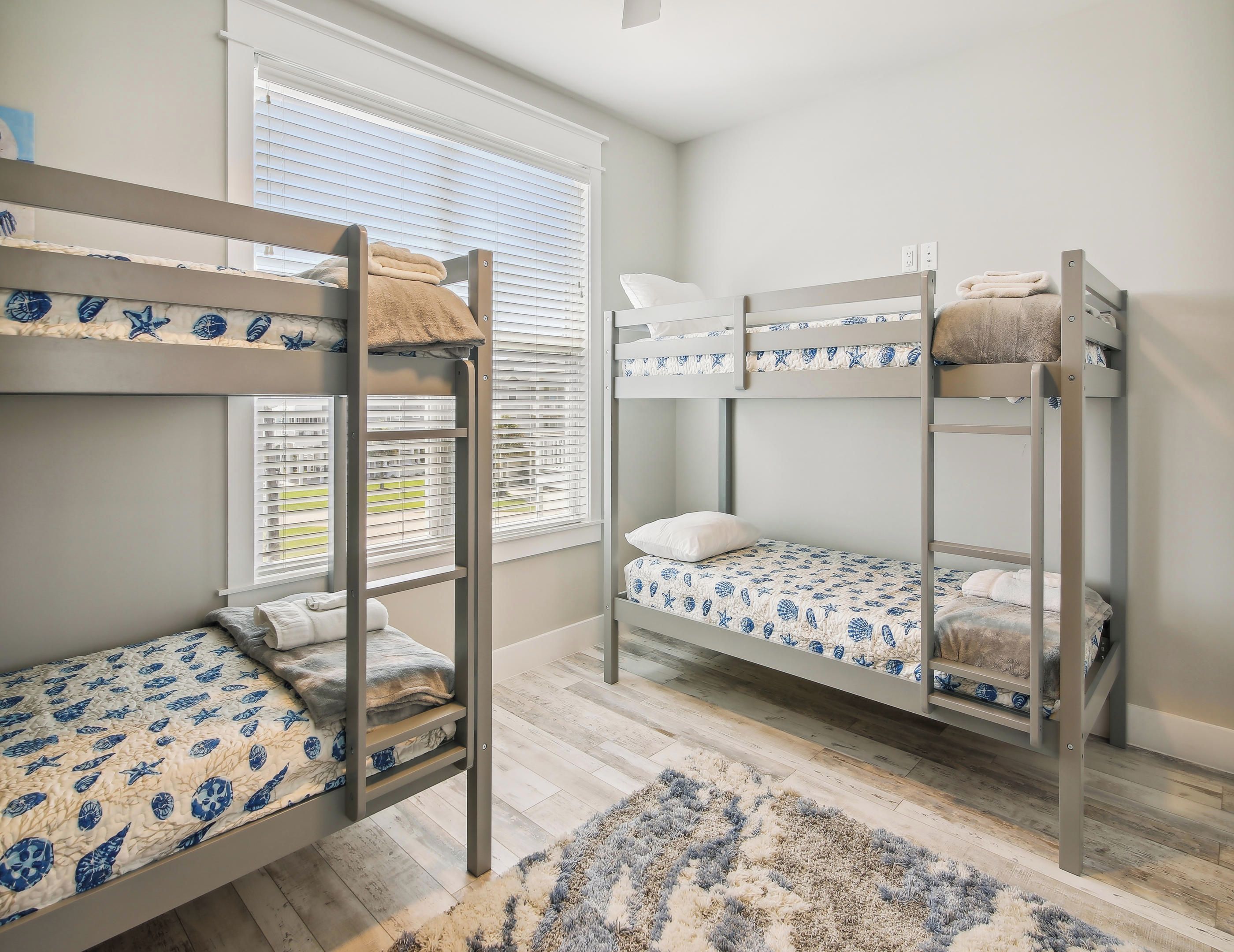 A room with bunk beds, a window with blinds, and a patterned rug.