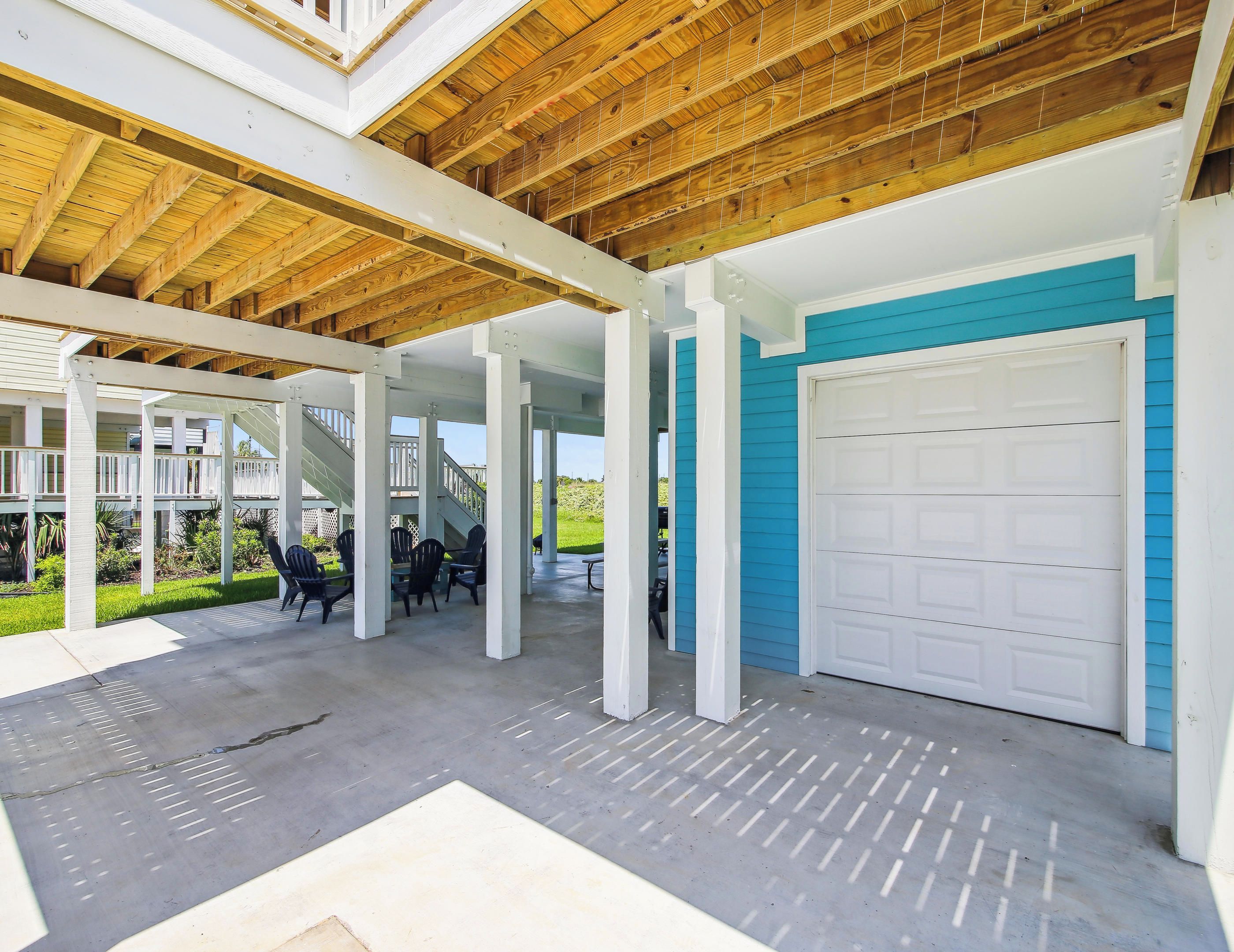 En overdækket terrasse med betongulv, hvide søjler og en blå garagedør.