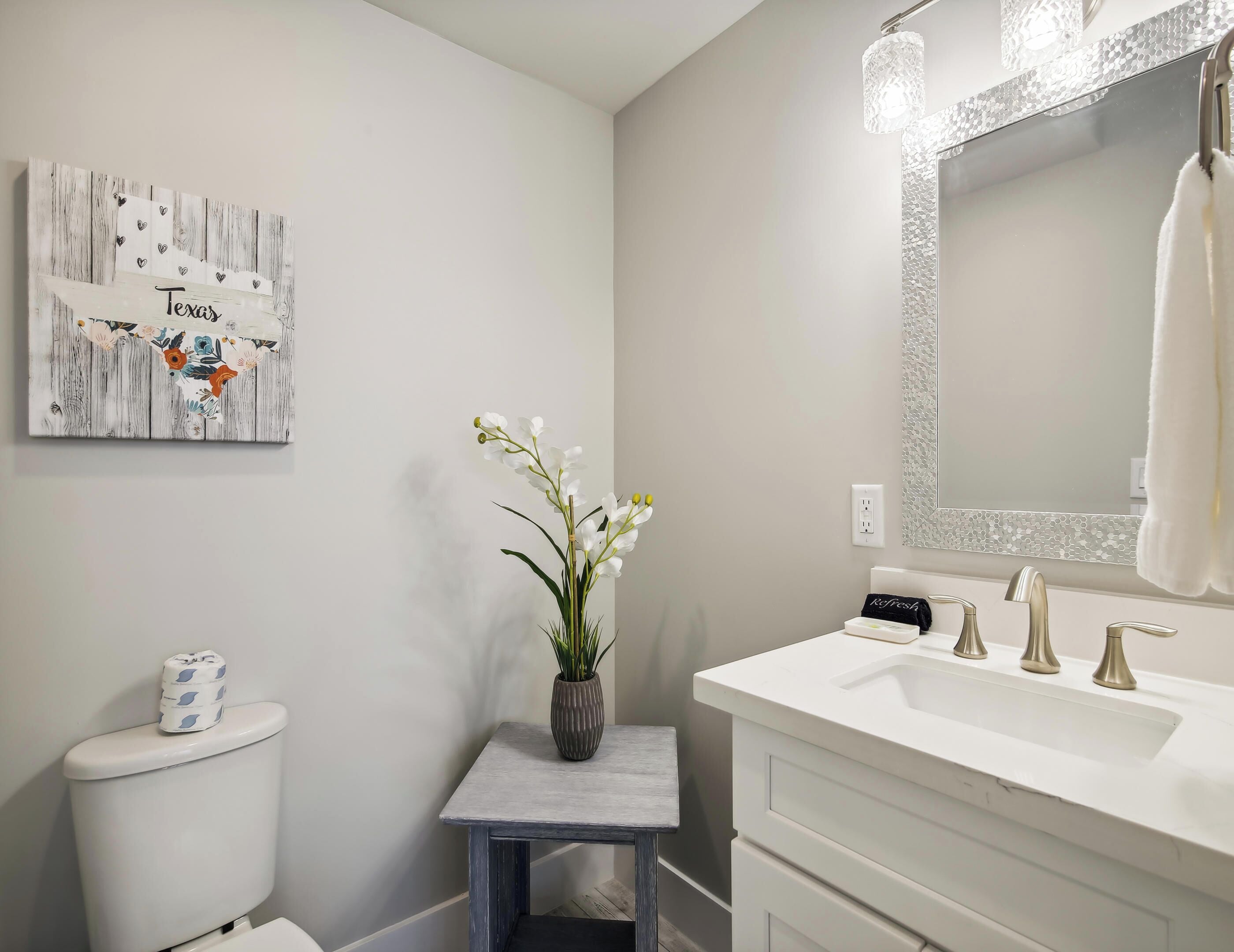 A bathroom with a white sink, a mirror with a textured frame, a toilet, and a decorative sign on the wall.