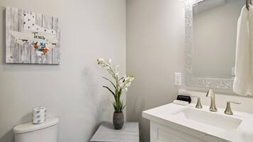 A bathroom with a white sink, a mirror with a textured frame, a toilet, and a decorative sign on the wall.