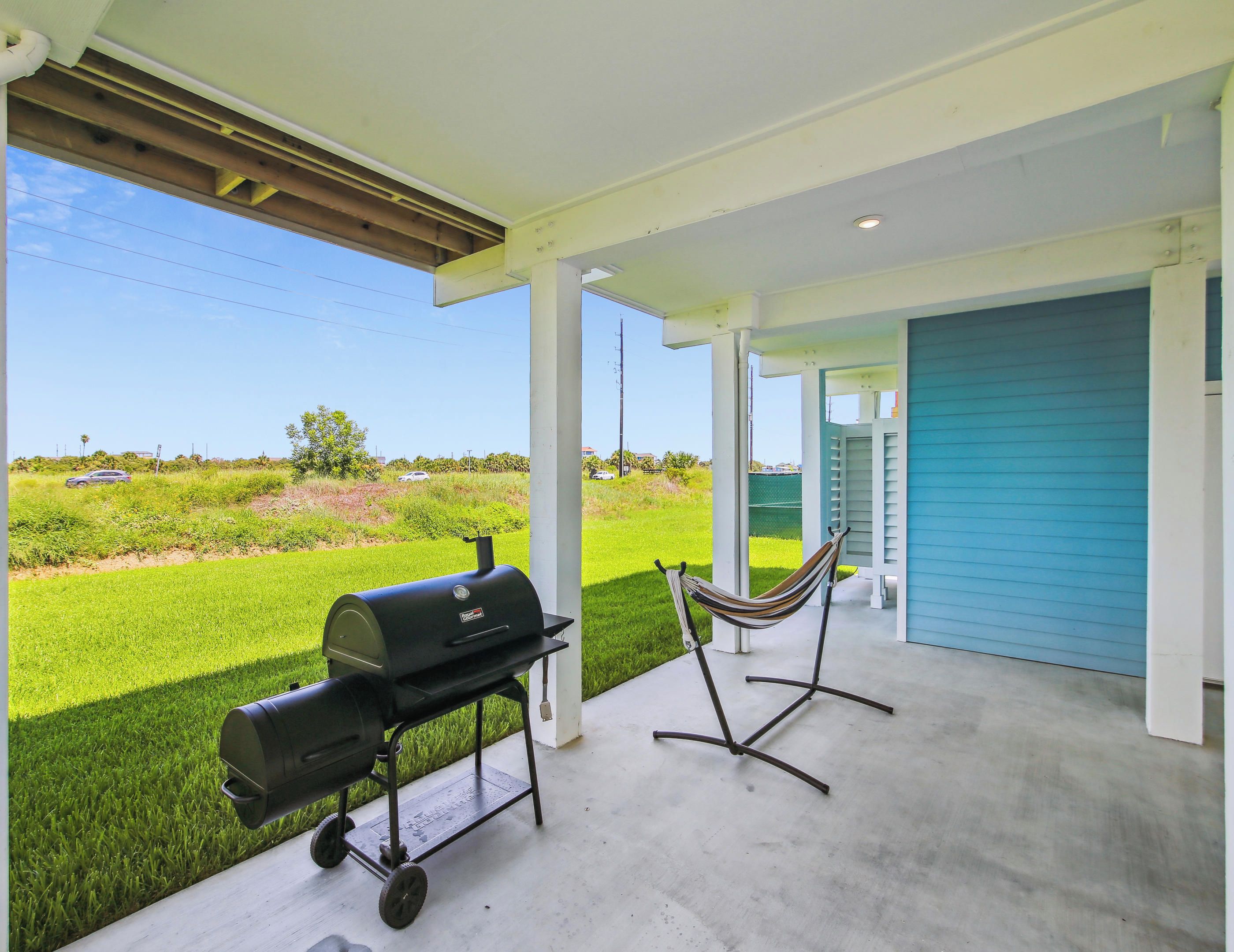 A covered patio area with a grill, a hammock, and a view of a green field.