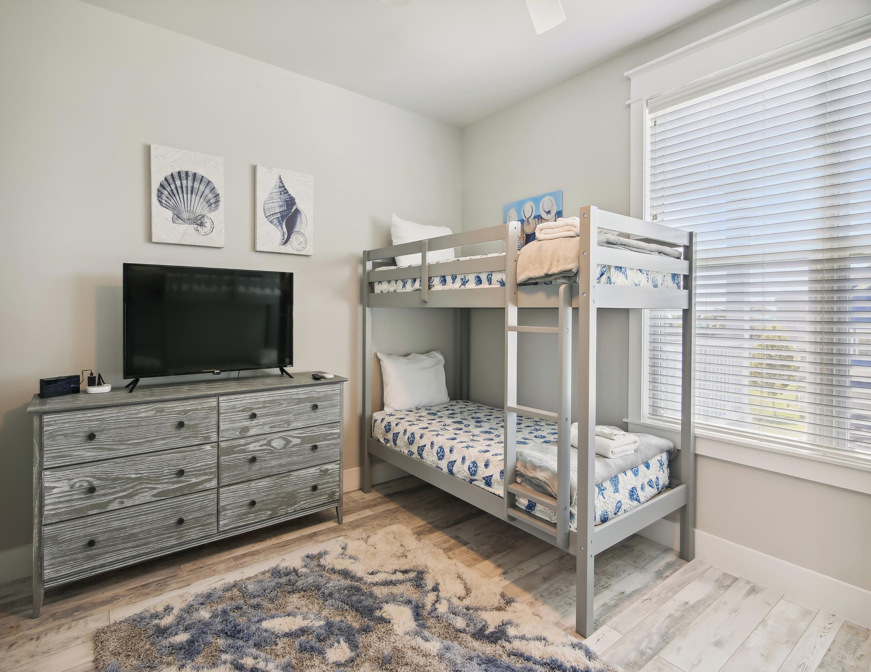A bedroom with a bunk bed, a TV, a dresser, and artwork on the wall.