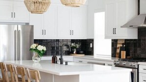 A modern kitchen with white cabinetry, a central island with bar stools, a stainless steel refrigerator, and a black tiled backsplash. - Good Life La Quinta!  PGA West! Mist/Pool/Spa/Putt (La Quinta)