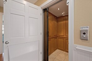 A hallway with a white door, a wooden elevator, and a wall-mounted elevator control panel.