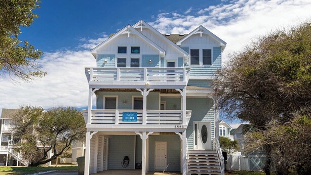 Una casa de dos pisos con cochera cubierta, balcón y un letrero que indica alquileres vacacionales de Coastal Carolina.