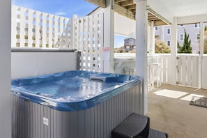 A hot tub with a wooden bench, a white fence, and a sign indicating spa rules.