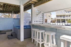 Ein überdachter Außenbereich mit Pool, weißen Barhocker und einer Holzterrasse.