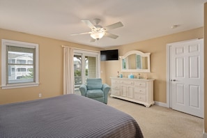 A bedroom with a bed, a ceiling fan, a dresser, a TV, and a door.