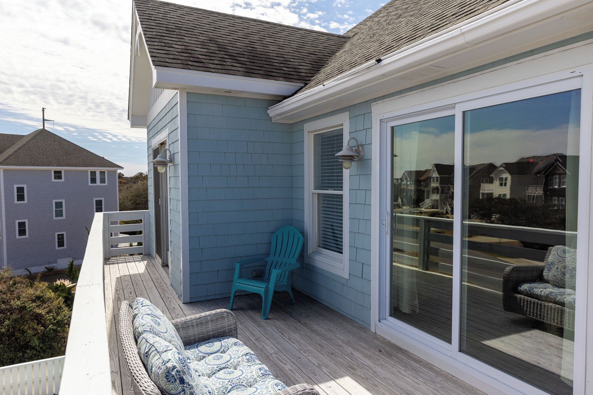 Un balcon avec un canapé en osier, une chaise turquoise et une porte vitrée donnant sur une terrasse.