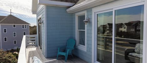Un balcon avec un canapé en osier, une chaise turquoise et une porte vitrée donnant sur une terrasse.