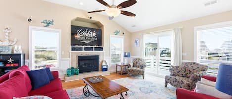 A living room with a fireplace, a ceiling fan, and a large window with a view.