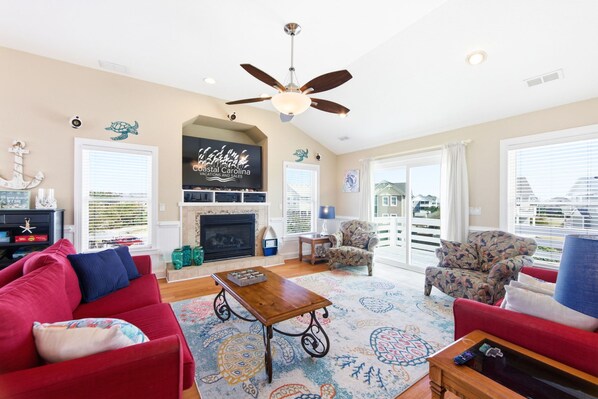A living room with a fireplace, a ceiling fan, and a large window with a view.
