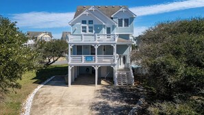Una casa de playa de dos pisos con balcón, un porche cubierto y una pequeña escalera que lleva a la entrada.