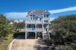 A two-story beach house with a balcony, a covered front porch, and a small staircase leading to the entrance.