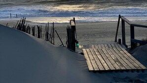 En strand med en træbro og et sandområde.
