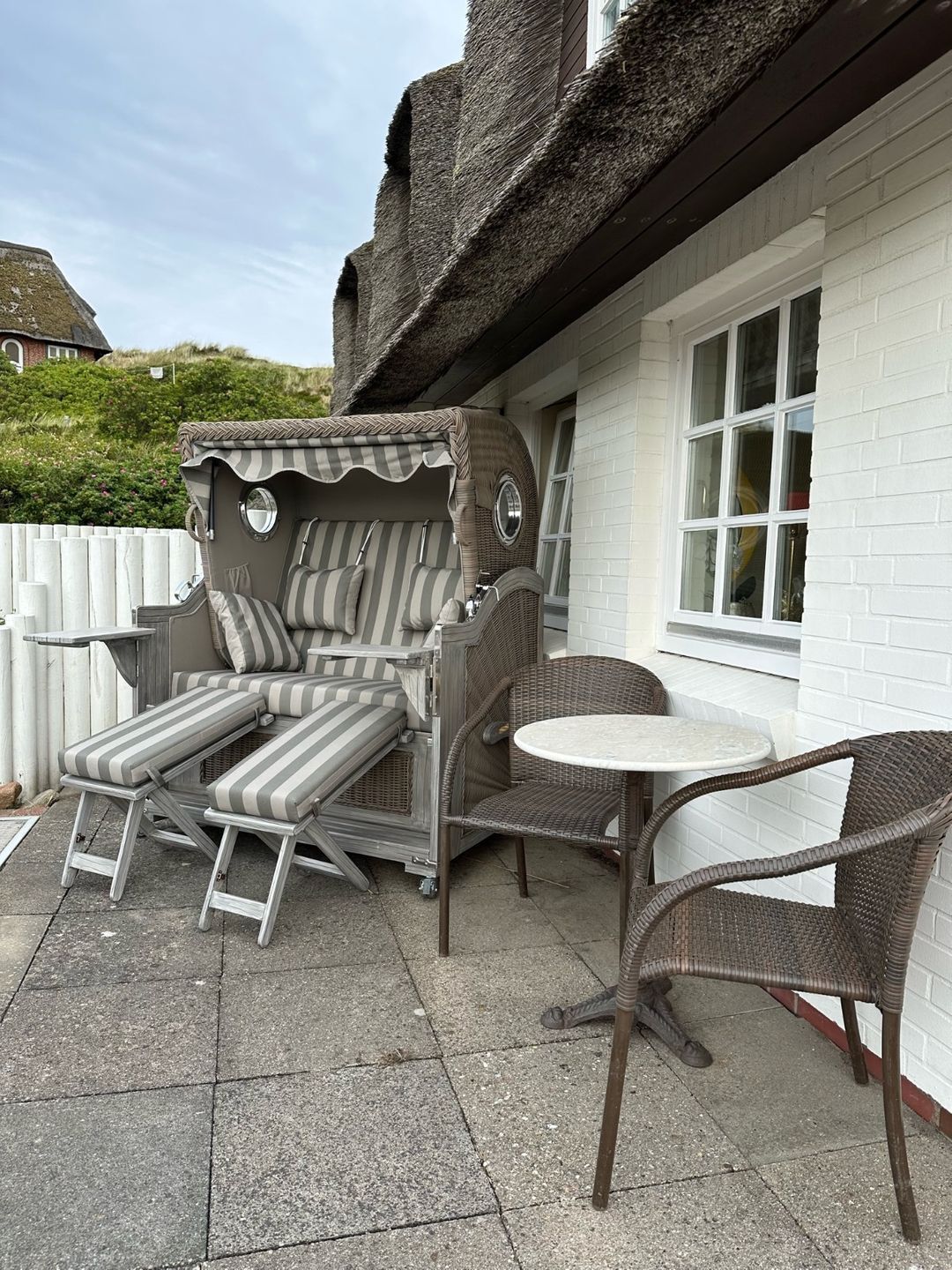 An outdoor seating area with a striped sofa, a round table, and wicker chairs.