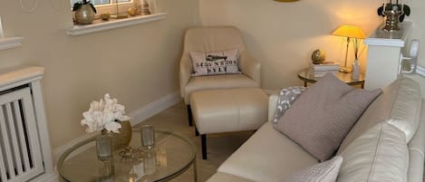 A living room with a white leather sofa, a round coffee table, a chair, a round mirror, and a window with curtains.