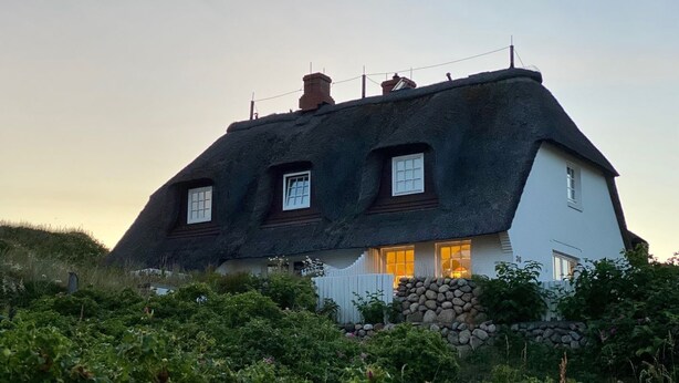 Et traditionelt bindingsværkshus med tre vinduer og en stenvæg foran.
