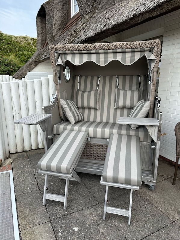 Un espace extérieur aménagé, abrité et doté d’un canapé à rayures et de deux fauteuils assortis, d’une petite table et d’un panier en osier.